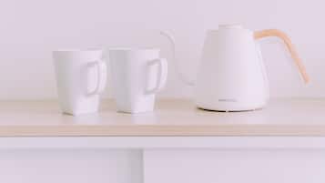 A white electric kettle and two white mugs on a light-colored countertop.