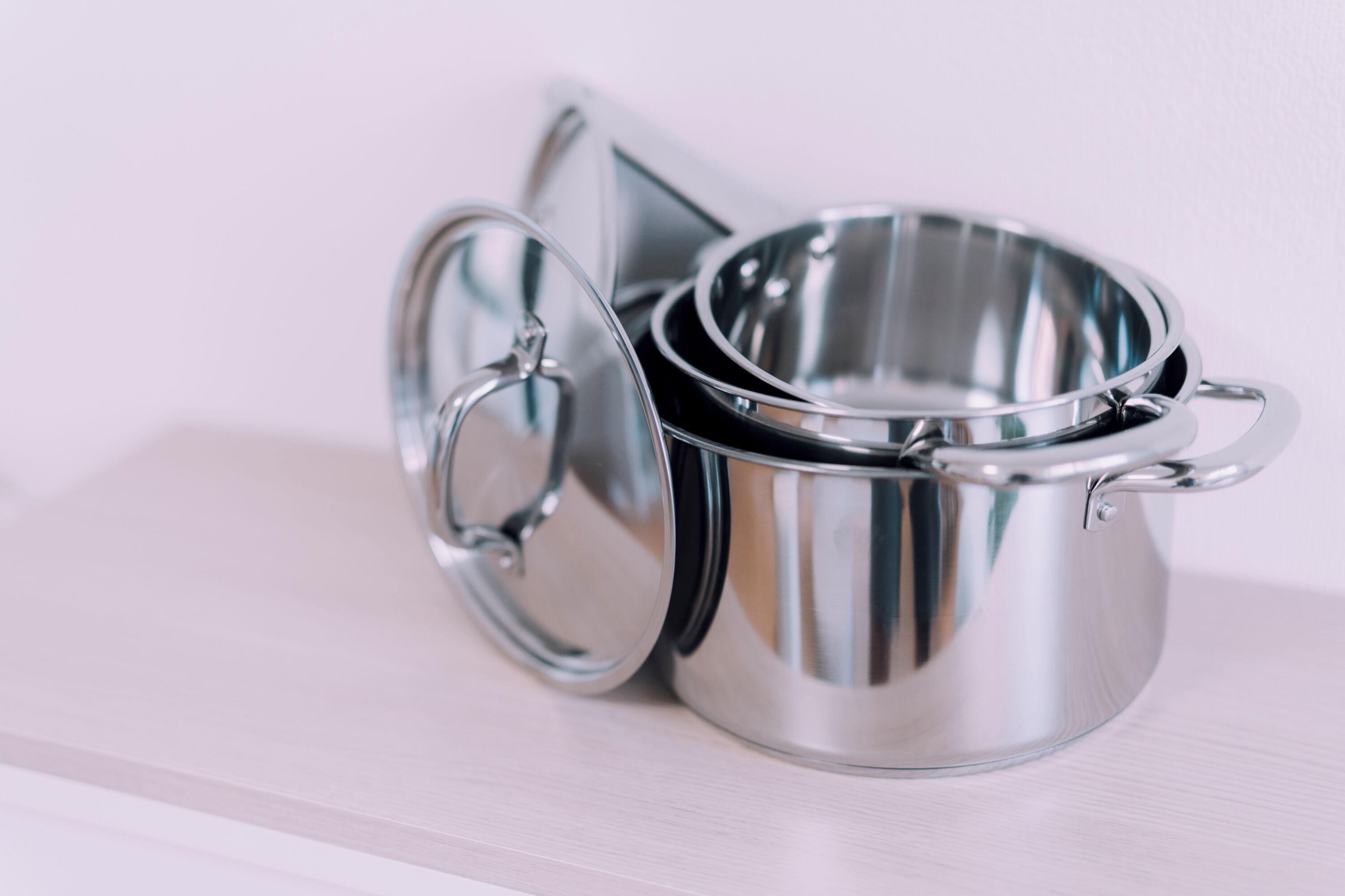 Utensilios de cocina de acero inoxidable con tapas, incluyendo una olla y una sartén, sobre una superficie de madera.