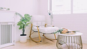 Ein Zimmer mit einem weißen Schaukelstuhl, einem kleinen runden Tisch und einem Blumentopf.