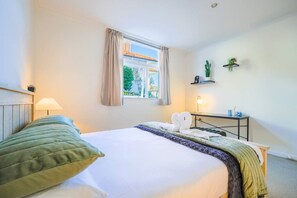 A hotel room with a bed, a desk, a lamp, and a window with curtains. - Charming 1-Bedroom Home in Prestigious Orakei (Auckland)