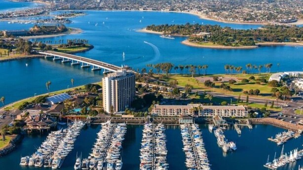 Un puerto deportivo con numerosas embarcaciones amarradas, un puente y un edificio grande de diseño moderno.