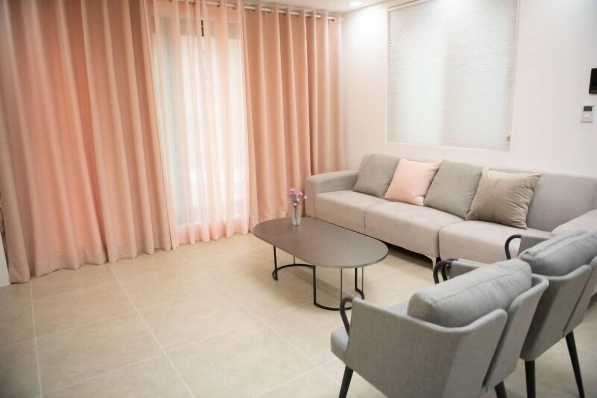 Ein Wohnzimmer mit einer Couch, zwei Sesseln, einem Couchtisch und einem Fenster mit Jalousien.