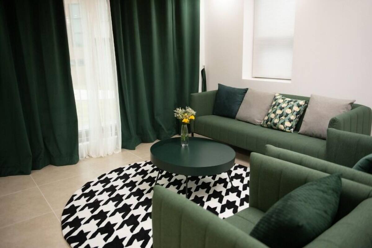 Ein modernes Wohnzimmer mit einem grünen Sofagarnitur, einem runden Couchtisch und einem gemusterten Teppich.