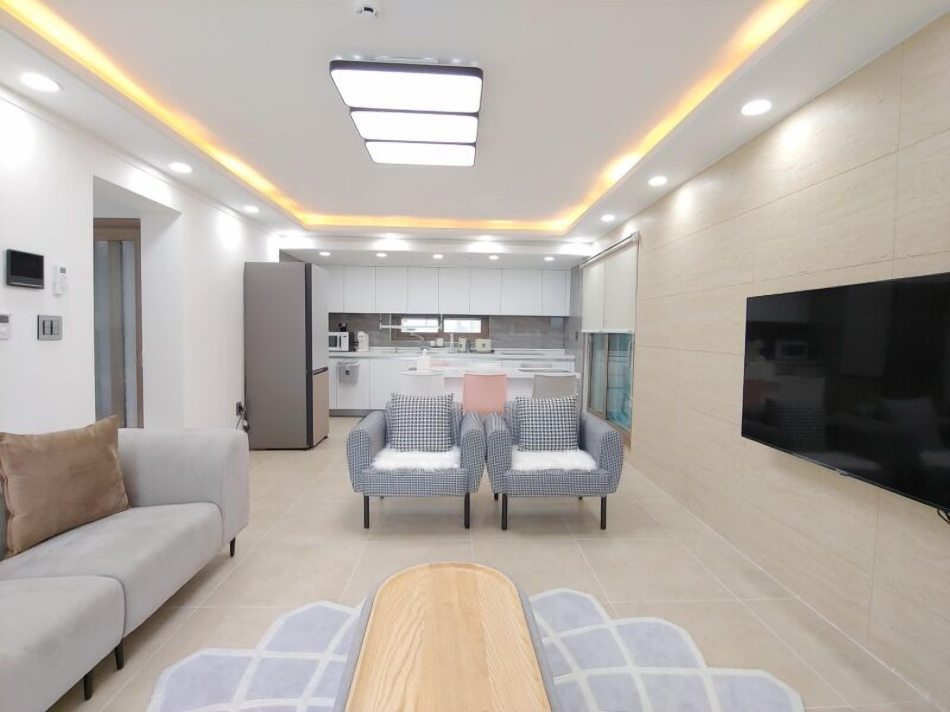 A modern living room with a sofa, two armchairs, a coffee table, and a TV mounted on the wall.