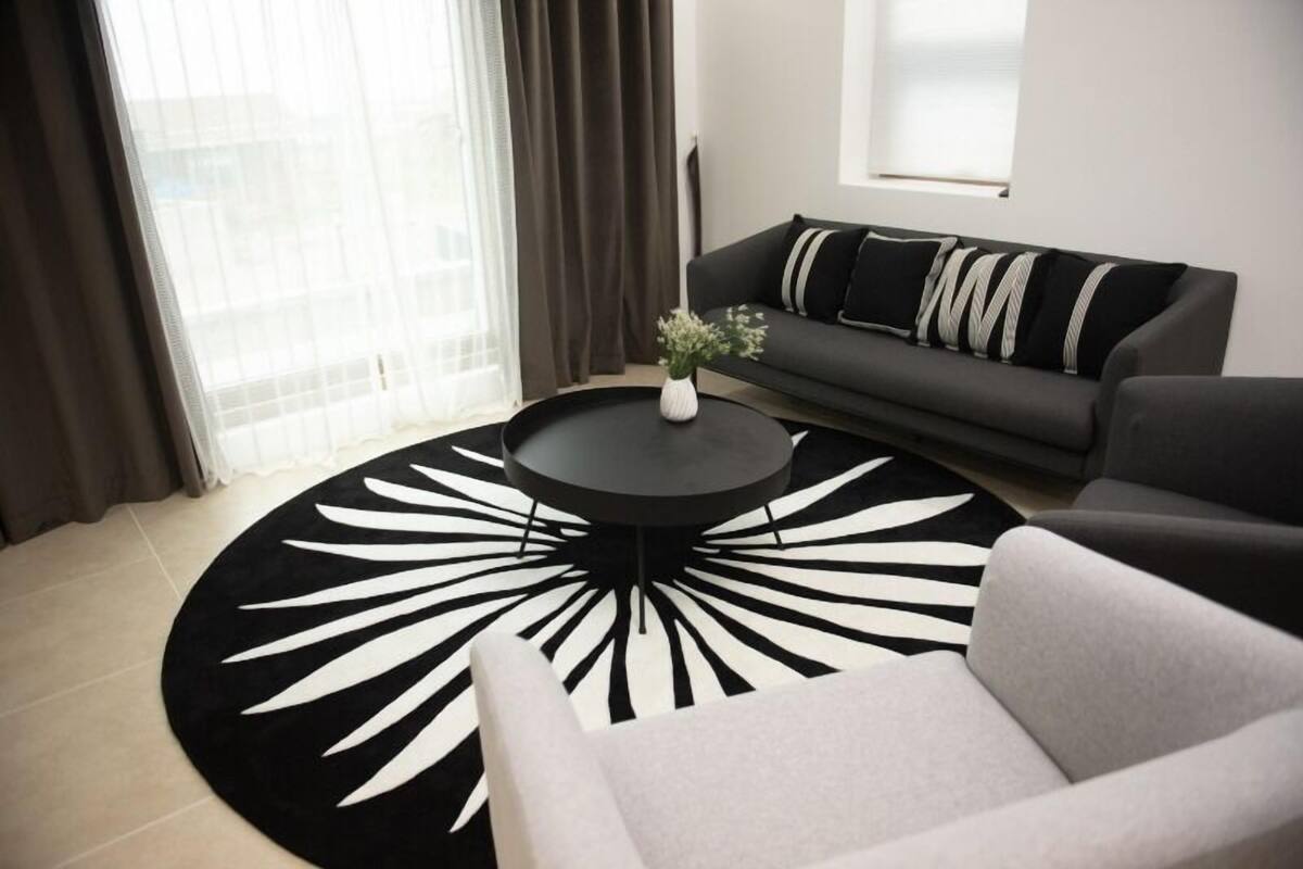 Ein modernes Wohnzimmer mit einem runden Couchtisch, einem grauen Sofa mit gestreiften Kissen und einem schwarz-weißen Teppich.