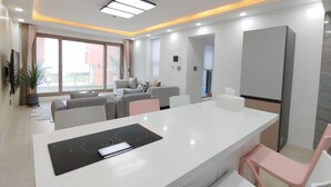 Een moderne woonkamer met een grote witte eettafel, een geïntegreerd keukenhoek met fornuis en een zithoek met een bank en stoelen.