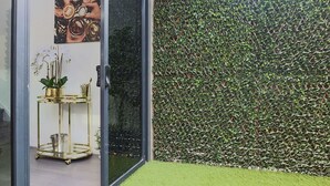 A modern interior with a glass door, a gold-framed table with a potted plant, and a green hedge outside. - Rare Loft Style Penthouse Bourke St Mall + Parking (Melbourne)