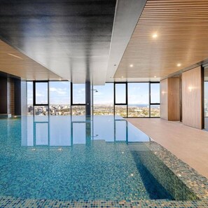 Une piscine intérieure moderne avec des parois en verre transparent, un sol carrelé et une vue sur la ville.