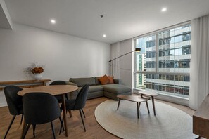 A modern living room with a sofa, a dining table, chairs, a coffee table, and a large window with a city view.