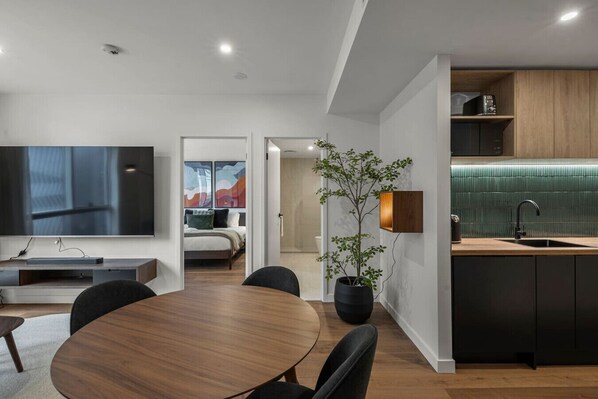 Habitació d'hotel moderna amb zona de dinar, televisió, planta i cuina amb un frontó verd.