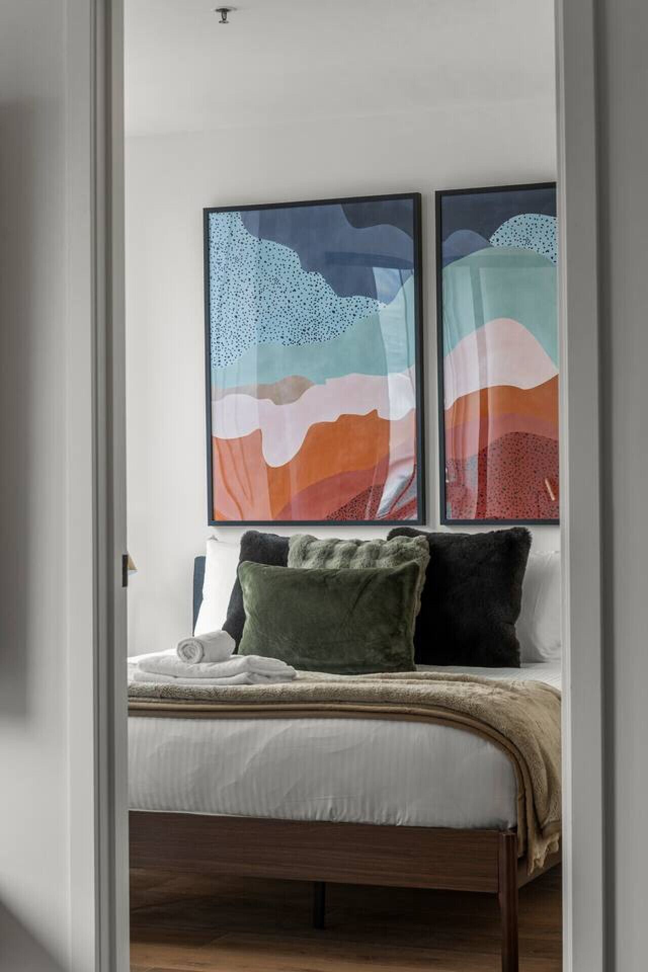 A bedroom with a bed, pillows, and two abstract paintings on the wall.