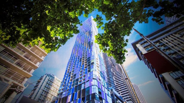 Een hoog gebouw met een moderne glazen gevel, omgeven door bomen en andere gebouwen.