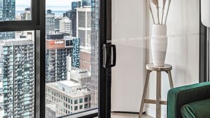 Een modern appartement met grote ramen, een groene bank, een witte vaas met pluimveedergras en uitzicht over de stad.