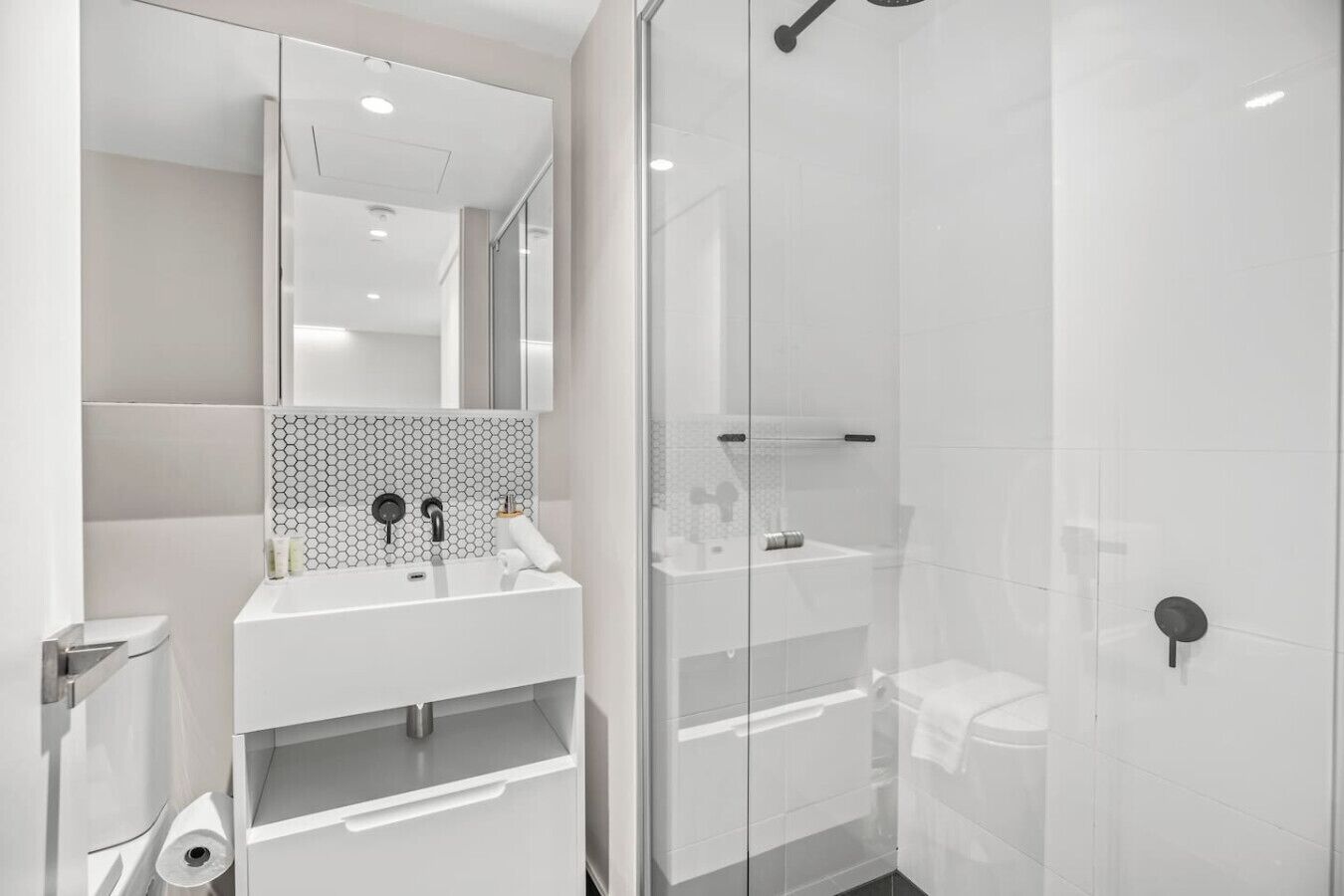 A modern bathroom with a glass shower enclosure, a white sink with a hexagonal tile backsplash, and a mirror above the sink.