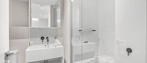 A modern bathroom with a glass shower enclosure, a white sink with a hexagonal tile backsplash, and a mirror above the sink.