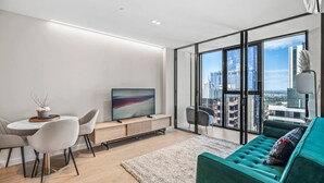 Een moderne woonkamer met een bank, televisie en een eethoek, met grote ramen en uitzicht over de stad.