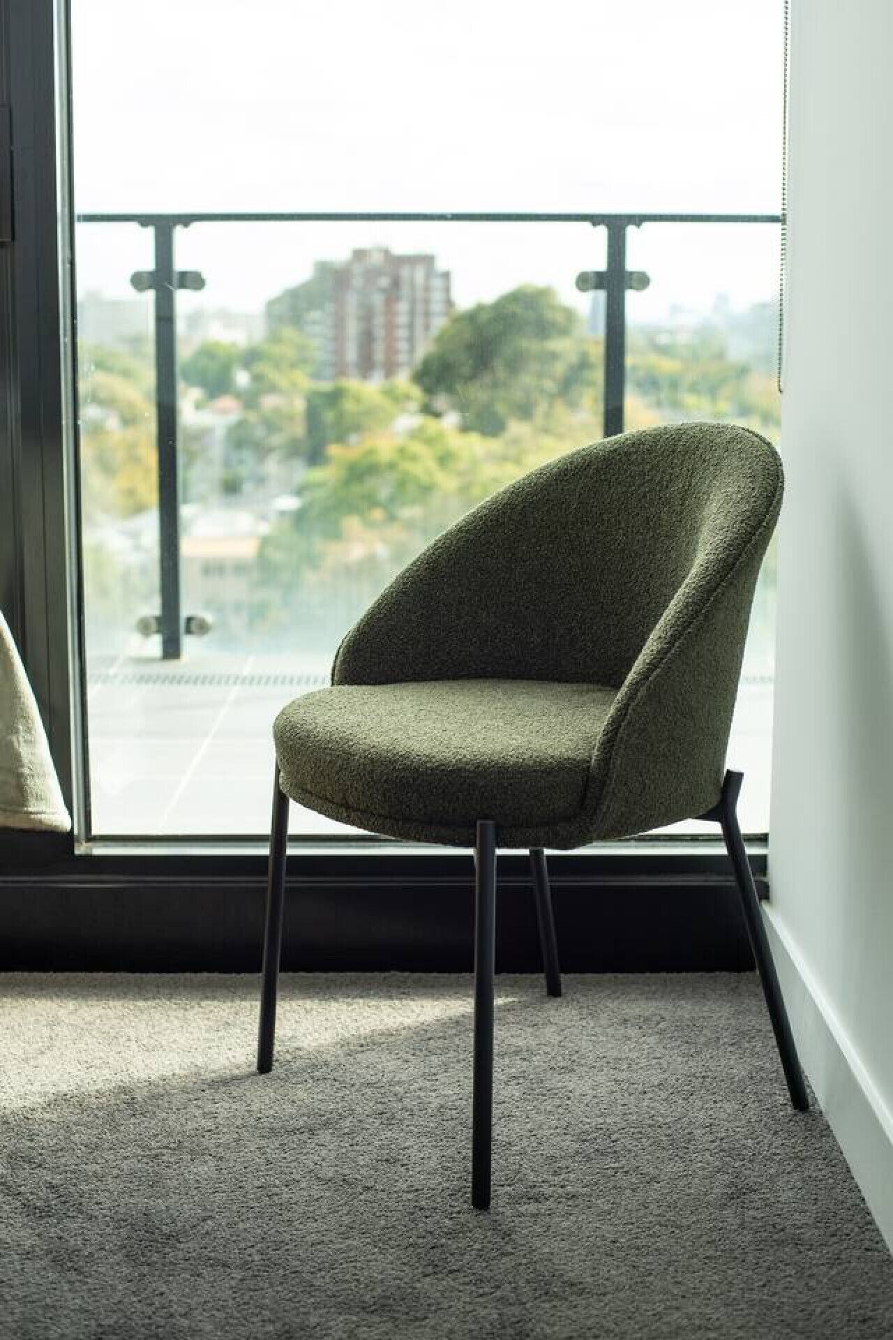A chair with a textured fabric, positioned in front of a window with a view of buildings and trees.
