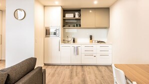 Une cuisine compacte avec des meubles blancs, un four à micro-ondes, un évier et un petit plan de travail.