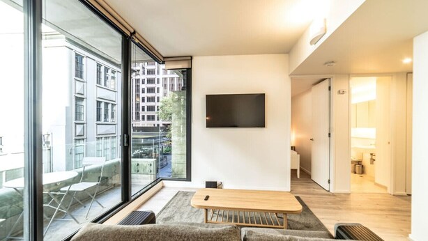 Un salon moderne doté d’une grande fenêtre, d’un téléviseur à écran plat, d’une table basse en bois et d’un canapé.