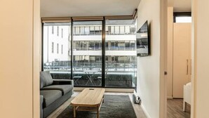 Un appartement moderne comprenant un espace de vie, un canapé, une table basse, un téléviseur et une vue sur un immeuble.