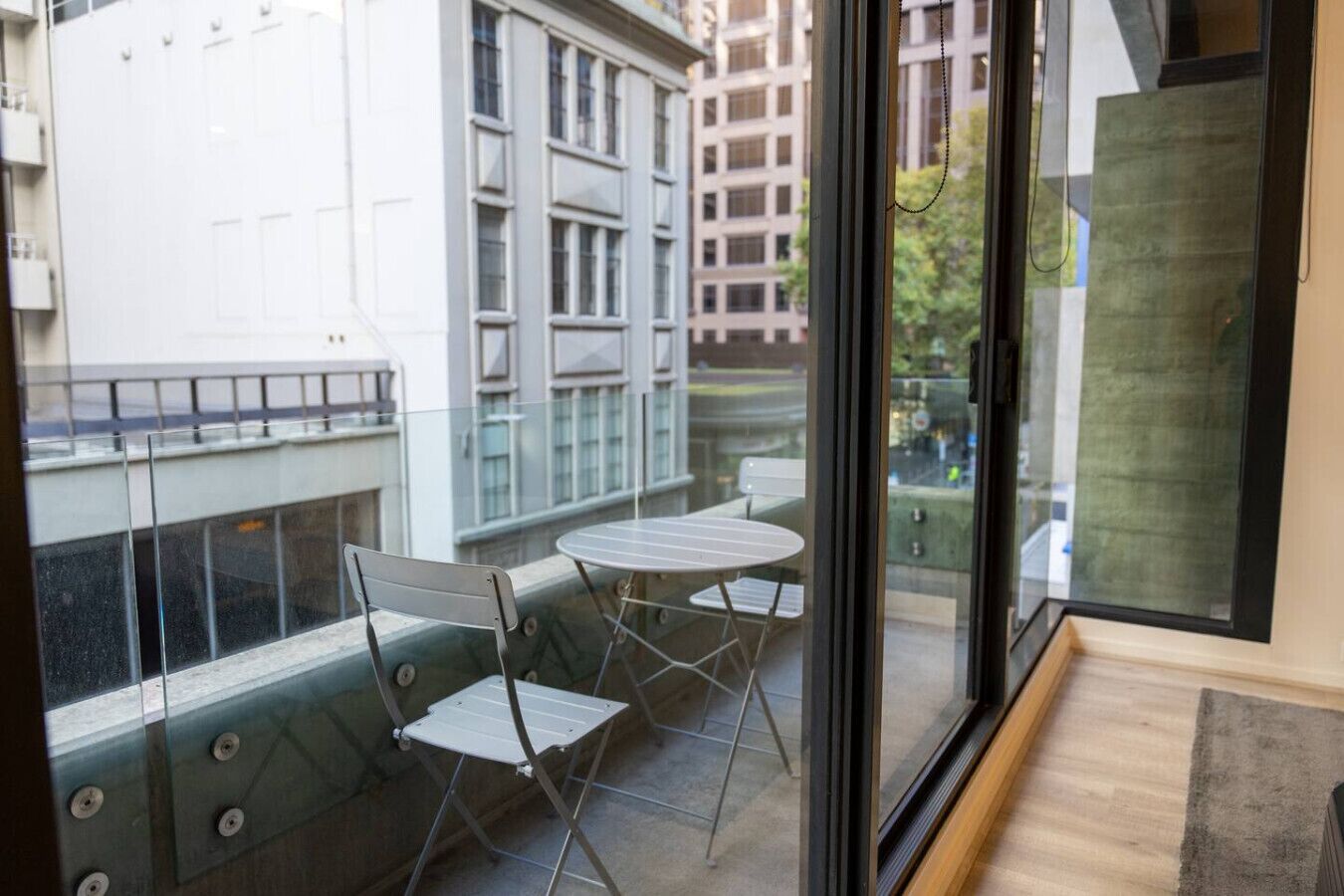 A balcony with a table and chairs, a glass door, and a view of buildings.