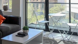 Un salon moderne avec un canapé, une table basse et une vue sur un bâtiment historique, visible à travers de grandes fenêtres.