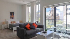 Un salon moderne comprenant un canapé, une petite table, un lit et de grandes fenêtres donnant sur la ville.