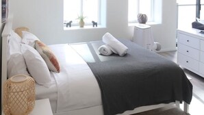 Une chambre à coucher moderne, avec un lit, des tables de chevet, une commode et de grandes fenêtres.