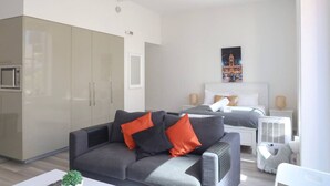 Un salon moderne comprenant un canapé, un lit, un coin cuisine et une œuvre d’art accrochée au mur.