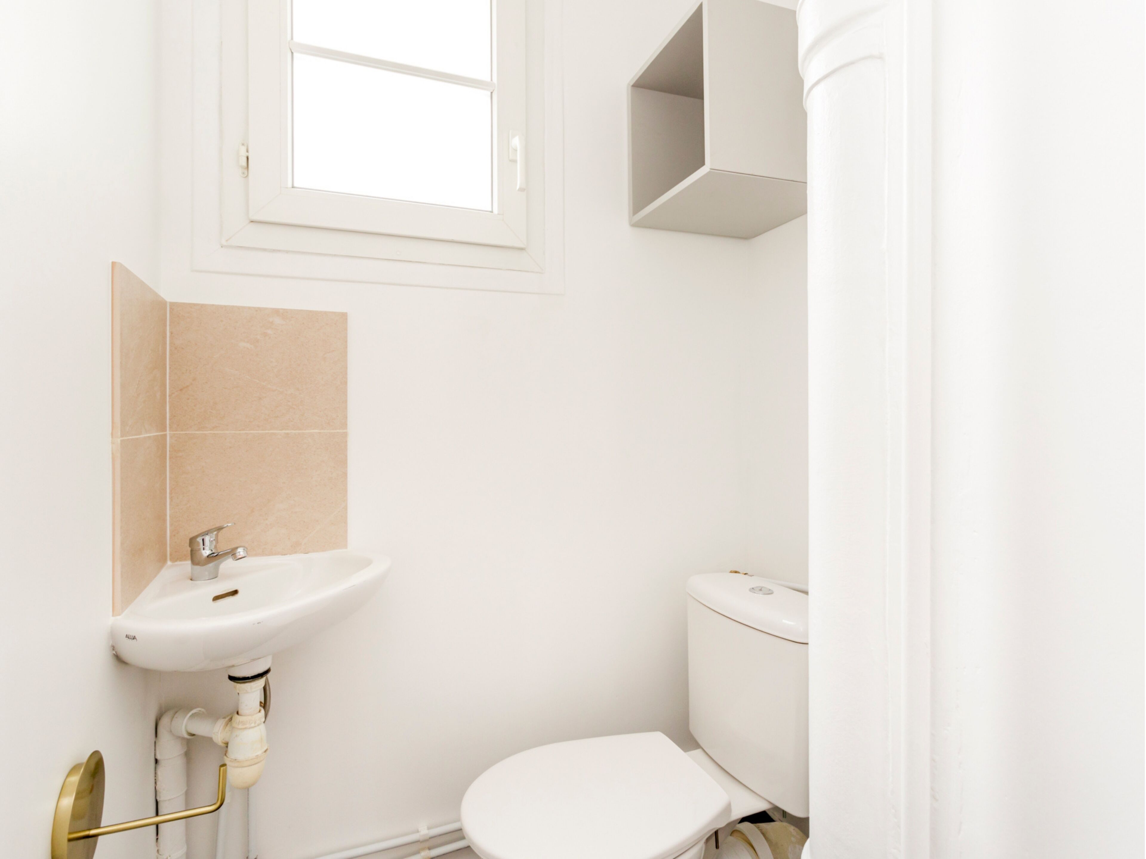 A small, clean bathroom with a white sink, toilet, and a window above the sink.