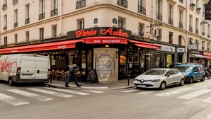 A multi-story building with a curved corner facade, featuring a restaurant named "Paris Auber" with a red awning. - Family Suites Caumartin I-II (Paris)