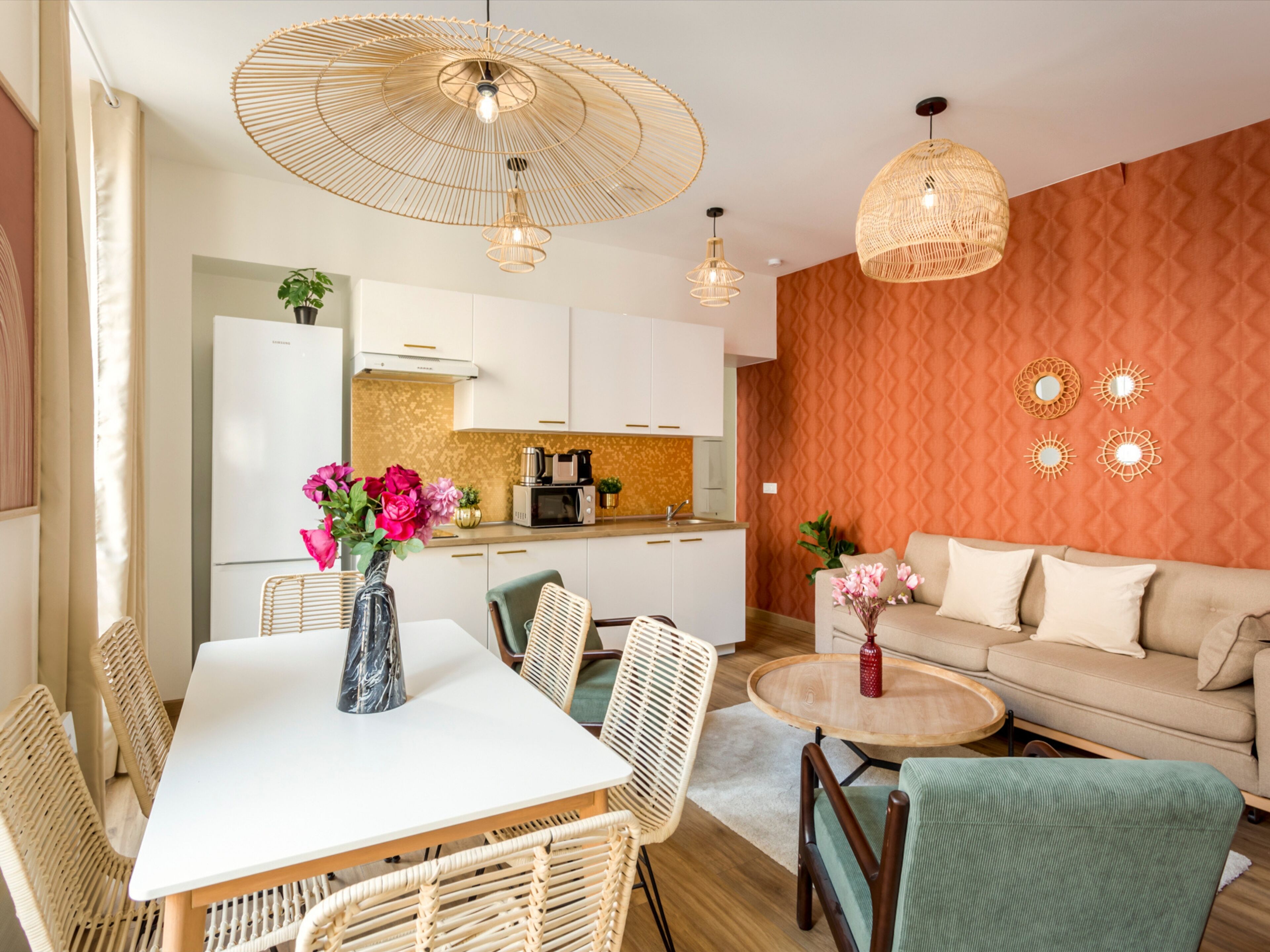 Una cocina moderna con armarios blancos, microondas y cafetera. Hay una mesa de comedor con sillas y un jarrón de flores.