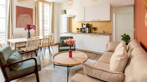 A modern living room with a sofa, chairs, a dining table, and a kitchen area with cabinets and appliances. - Family Suites Caumartin I-II (Paris)