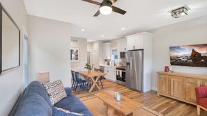 A modern living room with a sofa, coffee table, and a dining area with chairs. - Navvy Town Neighborhood at Heritage Harbor (Ottawa)