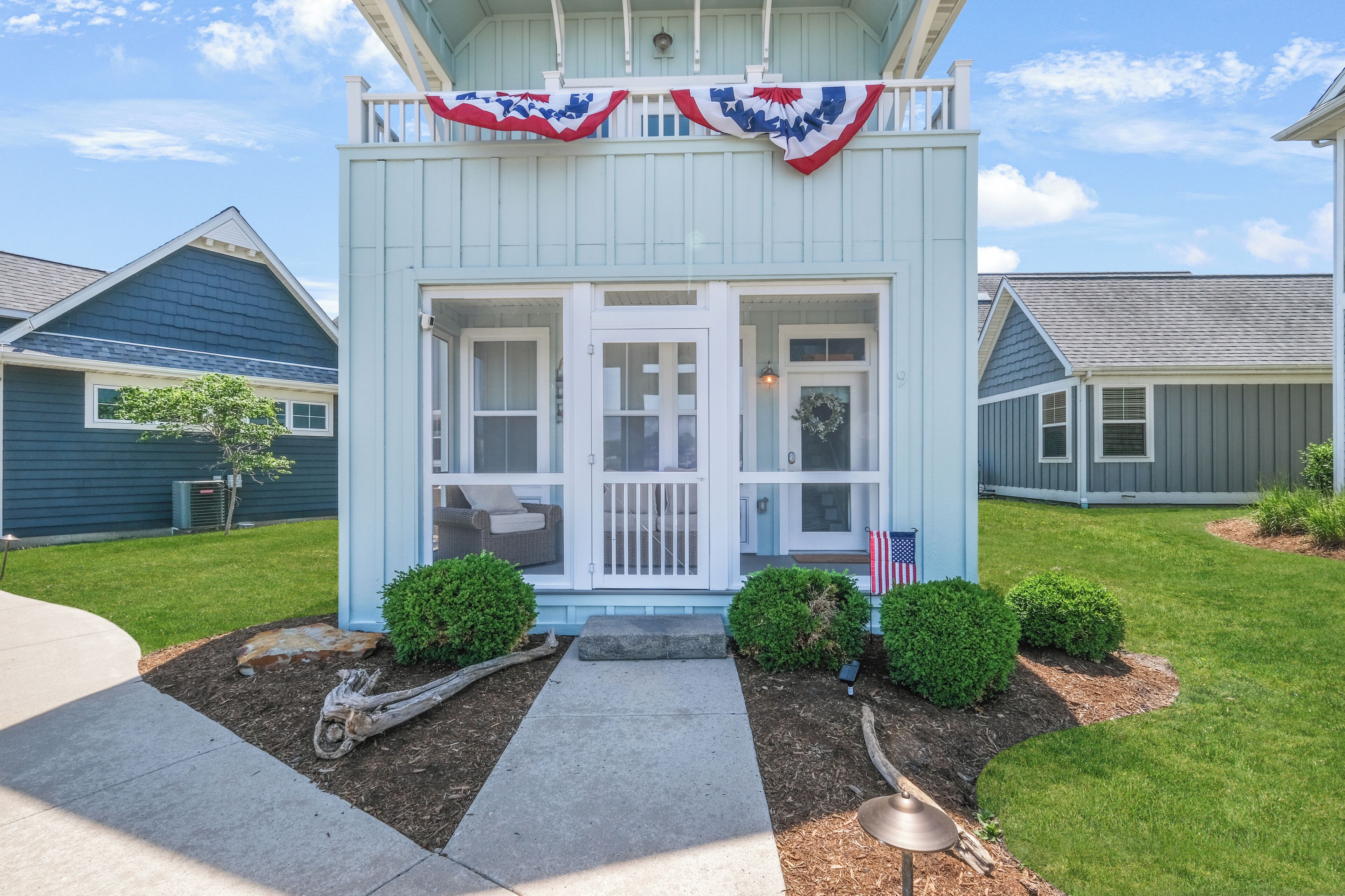 A light blue house with a porch, a front door, and a small garden area with a pathway leading to the door.