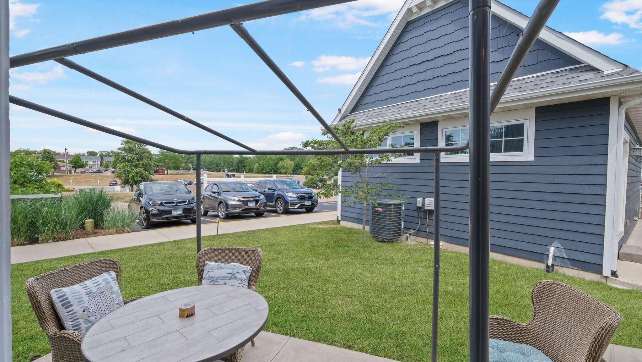 A covered patio with wicker furniture, a table, and a view of parked cars and a house.