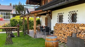Eine hölzerne Sitzgelegenheit im Freien mit Tisch, Stühlen, einem Fass und einem Holzstapel.