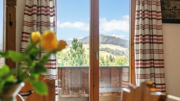 Ein Zimmer mit Holzbalkon, Vorhängen und Blick auf eine grüne Landschaft.