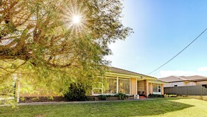 A residential house with a well-maintained lawn, a large tree providing shade, and a clear sky. - Emu Point Beach Cottages (Emu Point)