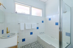A bathroom with a bathtub, a glass shower enclosure, a sink with a decorative basin, and a window with blinds.