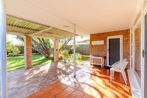 A covered patio area with a brick wall, a door, and a table with chairs.