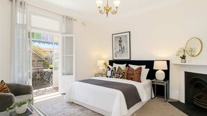 Une chambre à coucher avec un lit, une cheminée, une table de chevet, une chaise et un balcon.