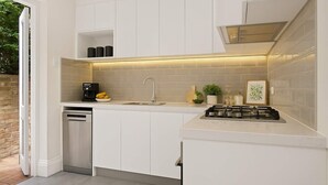 Une cuisine moderne avec des meubles blancs, un lave-vaisselle encastré, une cuisinière à gaz et un petit espace de comptoir agrémenté d’une machine à café et d’objets décoratifs.