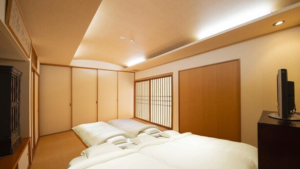 A traditional Japanese-style bedroom with tatami flooring, a low bed, sliding doors, and a television on a stand. - Shukubou Shinsen (Kanazawa)
