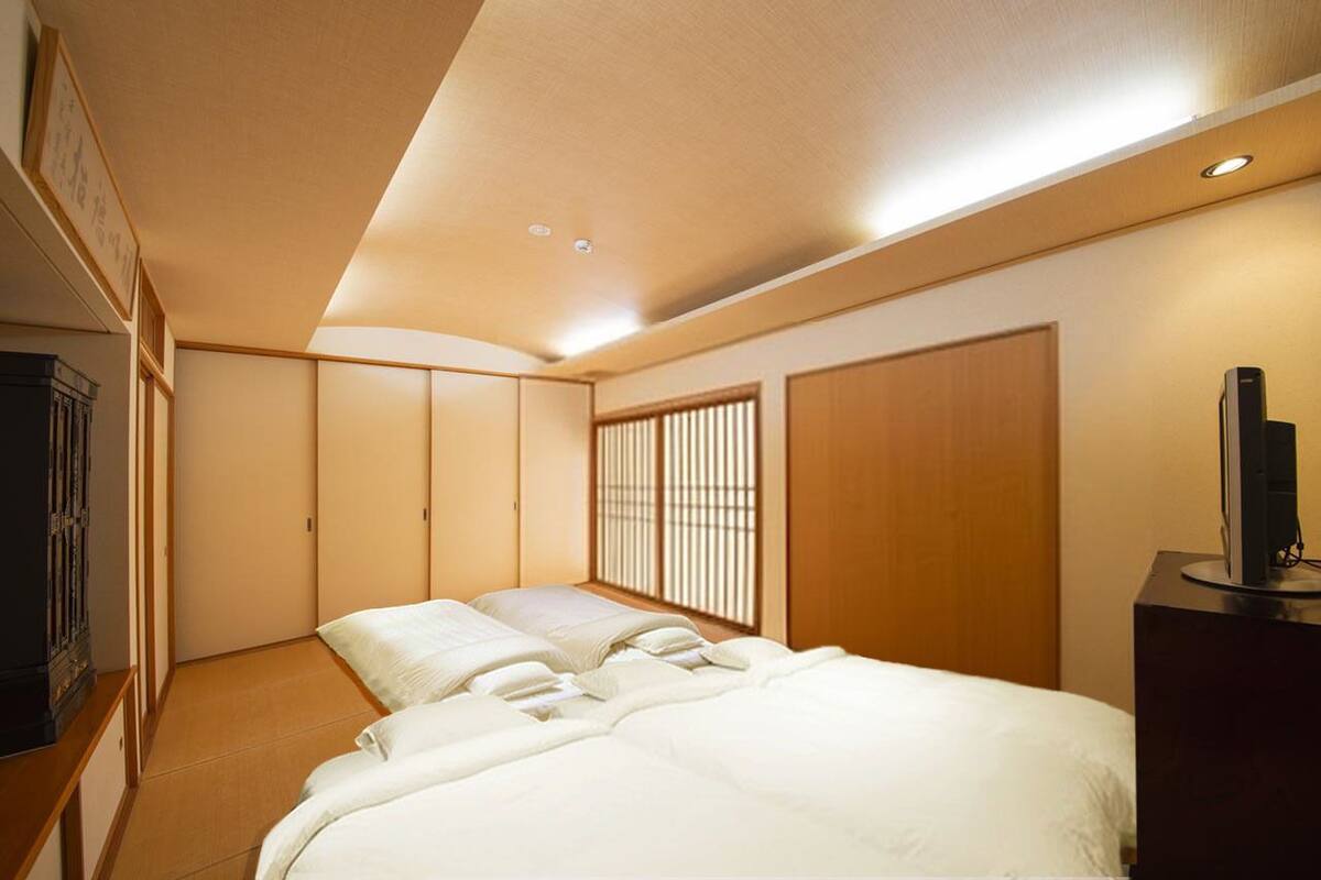 A traditional Japanese-style bedroom with tatami flooring, a low bed, sliding doors, and a television on a stand.