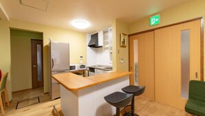 A compact kitchen with a wooden countertop, two bar stools, a microwave, and a stove. - Shukubou Shinsen (Kanazawa)