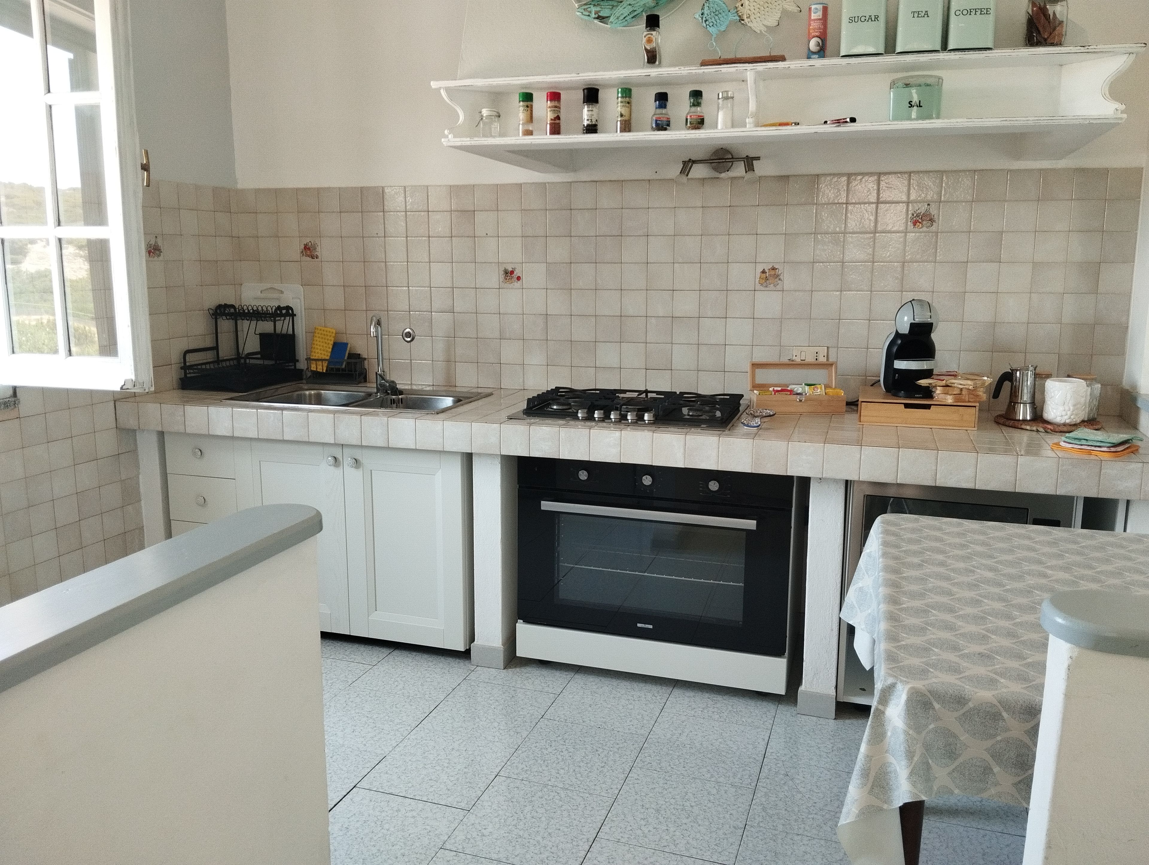 A kitchen with white cabinets, a gas stove, an oven, a sink, and a coffee maker.