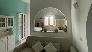 A living room with a sofa, a kitchen visible through an archway, and a dining area with a table and chairs.