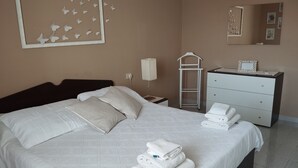 A neatly made bed with pillows and folded towels, a bedside table with a lamp, a dresser, and a wall-mounted mirror.
