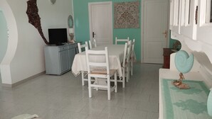 A dining area with a white table and chairs, a small cabinet with a television, and decorative wall art.
